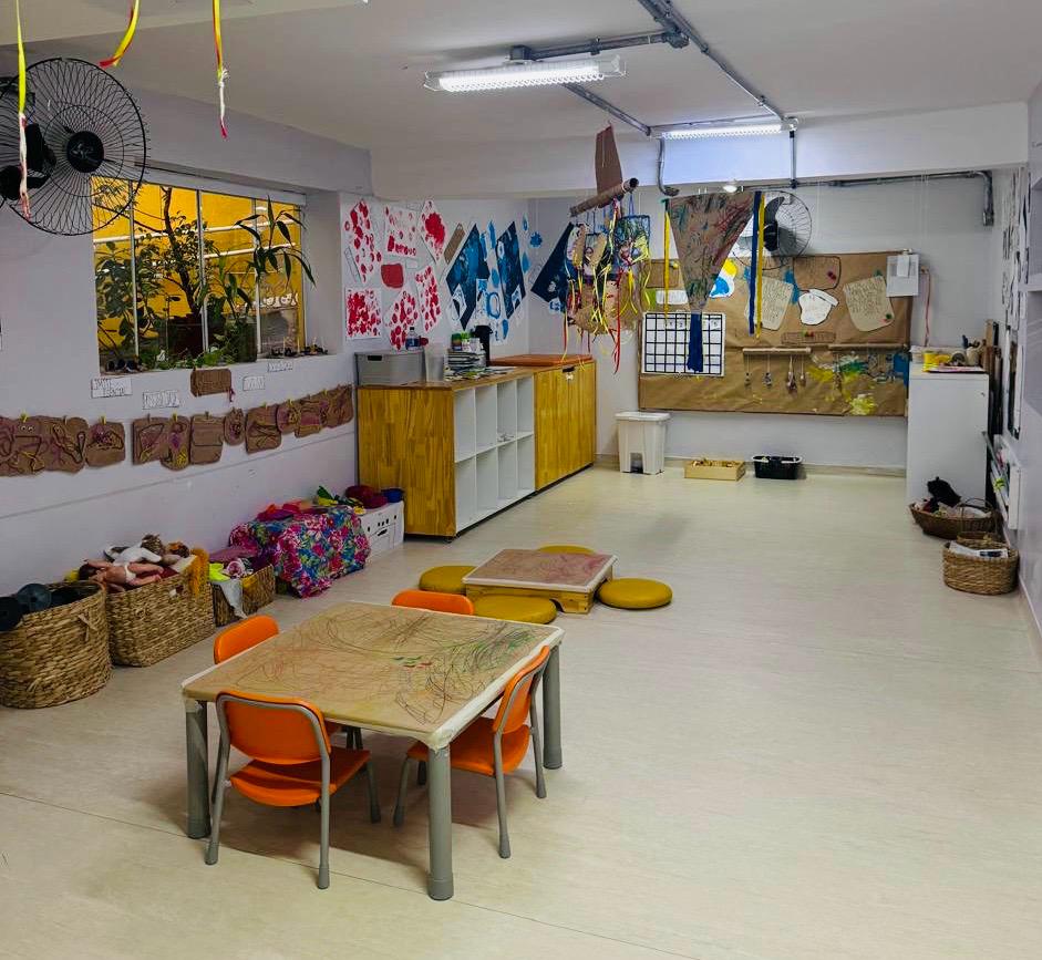 Ateliê com mesas, produções das crianças e cestos de materiais